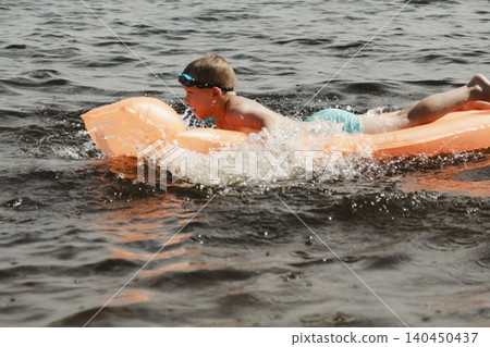little boy joyfully plays orange inflatable mattress river, creating bright splashes around him. image conveys carefree joy and energy childhood summer day. water activities childre, family vacations little boy joyfully plays orange inflatable mattress river, creating bright splashes around him. image conveys carefree joy and energy childhood summer day. water activities childre, family vacations 140450437