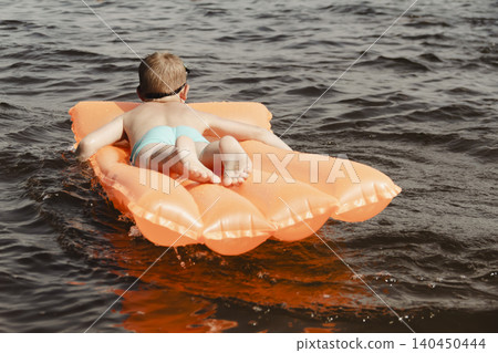 little boy joyfully plays orange inflatable mattress river, creating bright splashes around him. image conveys carefree joy and energy childhood summer day. water activities childre, family vacations little boy joyfully plays orange inflatable mattress river, creating bright splashes around him. image conveys carefree joy and energy childhood summer day. water activities childre, family vacations 140450444