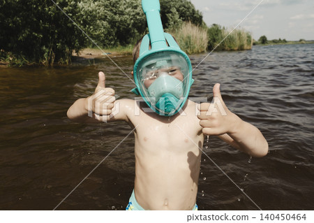 cheerful close up boy in shallow water wearing turquoise snorkeling mask. child gives two thumbs up, expressing delight approval. Family vacations, water safety, children's sports equipment, summer 140450464