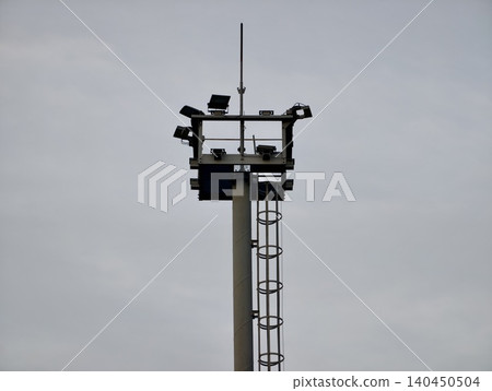 Tall lighting pole with mounted floodlights against cloudy sky Tall lighting pole with mounted floodlights against cloudy sky 140450504