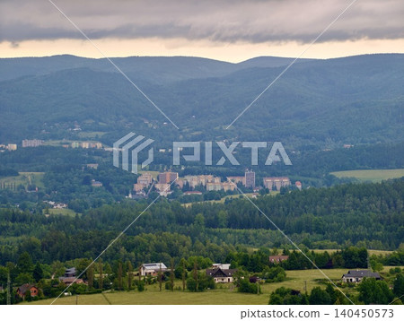 Mountain valley landscape with forested hills, village buildings, and cloudy sky Mountain valley landscape with forested hills, village buildings, and cloudy sky 140450573