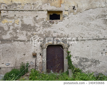 Weathered stone doorway with overgrown weeds and cracked plaster wall Weathered stone doorway with overgrown weeds and cracked plaster wall 140450666