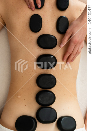 Top view of hot basalt stones placed along the spine during a spa massage treatment. Top view of hot basalt stones placed along the spine during a spa massage treatment. 140451474