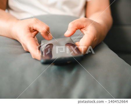 Close-up of Asian woman using a smartphone on a sofa at home, hands typing on a touchscreen, showing mobile communication, online browsing, digital lifestyle, social connection, and daily technology. Close-up of Asian woman using a smartphone on a sofa at home, hands typing on a touchscreen, showing mobile communication, online browsing, digital lifestyle, social connection, and daily technology. 140452664