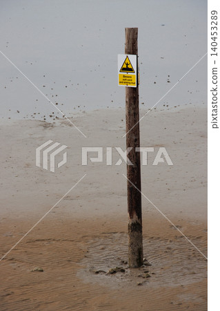 Danger sinking mud sign on pole in beach sand at low tide 140453289