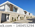 Modern luxury villas with minimalist architecture, natural stone walls, and expansive glass windows in a premium residential community under a bright blue sky. 140453294
