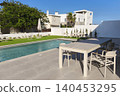 Modern backyard with a swimming pool, patio dining area, and landscaped garden under a clear blue sky, offering a relaxing outdoor lifestyle in a contemporary residential setting. 140453295