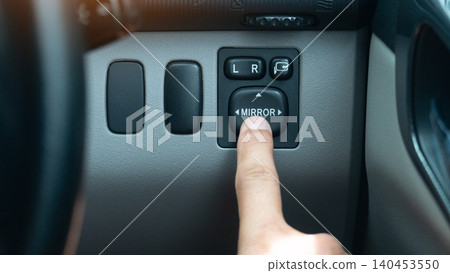 Close-up shot of a finger pressing the electric side mirror control switch button. On a car interior dashboard console panel illustrating driver adjustment adjustments. Close-up shot of a finger pressing the electric side mirror control switch button. On a car interior dashboard console panel illustrating driver adjustment adjustments. 140453550