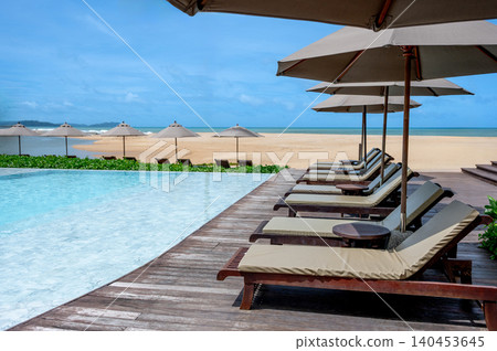 Luxury resort hotel with swimming pool and beach chairs or loungers under umbrellas Luxury resort hotel with swimming pool and beach chairs or loungers under umbrellas 140453645