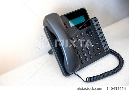 IP phone on the table in hotel room. Black landline telephone for communication support IP phone on the table in hotel room. Black landline telephone for communication support 140453654