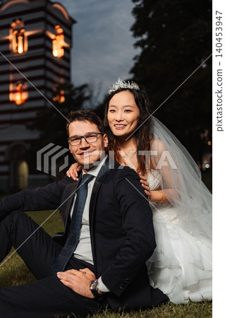 Interracial wedding couple smiling while sitting on grass 140453947