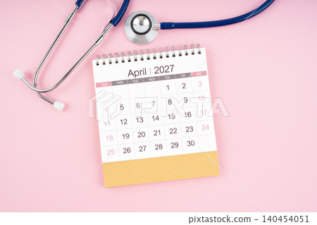 April 2027 desk calendar and Medical stethoscope on  pink background. 140454051