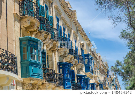 Traditional Maltese enclosed wooden balconies in turquoise and blue on limestone facade in Valletta Malta against bright blue sky. High quality photo 140454142