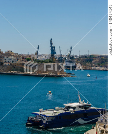 Passenger ferry catamaran in Grand Harbour Valletta Malta with shipyard cranes, historic fortifications and blue Mediterranean sea. High quality photo Passenger ferry catamaran in Grand Harbour Valletta Malta with shipyard cranes, historic fortifications and blue Mediterranean sea. High quality photo 140454143