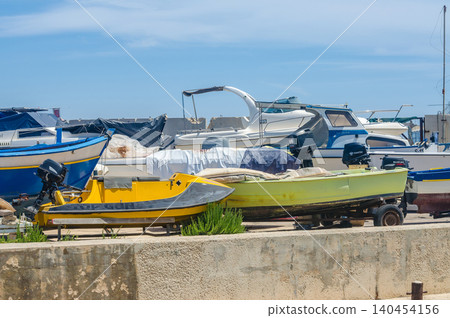Various small fishing boats and motorboats parked on land with outboard engines at a Mediterranean quayside boatyard under bright blue sky in summer High quality photo Various small fishing boats and motorboats parked on land with outboard engines at a Mediterranean quayside boatyard under bright blue sky in summer High quality photo 140454156
