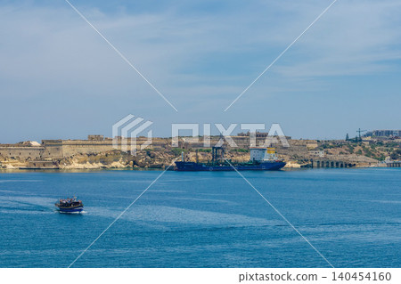 Cargo tanker ship moored near historic stone fortifications in Grand Harbour Valletta Malta with tourist boat on Mediterranean sea. High quality photo 140454160