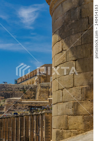 Ancient limestone fortification walls and bastion tower in Valletta Malta with historic arched architecture against blue sky. High quality photo Ancient limestone fortification walls and bastion tower in Valletta Malta with historic arched architecture against blue sky. High quality photo 140454163