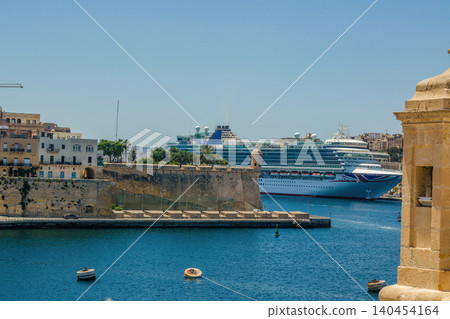 Large cruise ship docked in Grand Harbour Valletta Malta with historic stone fortifications and watchtower under clear blue sky. High quality photo 140454164