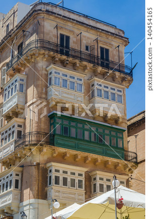 Traditional Maltese corner building with enclosed wooden gallarija balconies in green and white on limestone facade in Valletta Malta. High quality photo 140454165