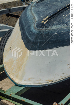 Close up of an old white and blue boat hull bottom with scratches and wear, resting upside down on a rusty trailer at a Mediterranean boatyard in sun High quality photo Close up of an old white and blue boat hull bottom with scratches and wear, resting upside down on a rusty trailer at a Mediterranean boatyard in sun High quality photo 140454174