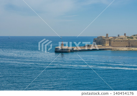 Scenic Mediterranean seascape with red lighthouse, historic limestone fortress, sailing boats and turquoise sea under bright blue sky at Grand Harbour Malta High quality photo Scenic Mediterranean seascape with red lighthouse, historic limestone fortress, sailing boats and turquoise sea under bright blue sky at Grand Harbour Malta High quality photo 140454176