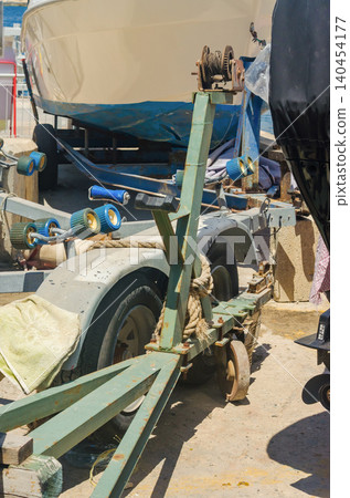 Boats parked on rusty steel trailers with blue rollers, manual winch and mooring ropes at a Mediterranean quayside boat storage yard under bright sun High quality photo Boats parked on rusty steel trailers with blue rollers, manual winch and mooring ropes at a Mediterranean quayside boat storage yard under bright sun High quality photo 140454177