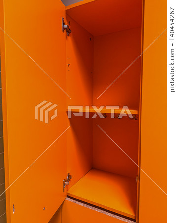 Bright orange open empty locker cabinet with inner shelves and metal hooks in a modern gym, school, or workplace changing room. Bright orange open empty locker cabinet with inner shelves and metal hooks in a modern gym, school, or workplace changing room. 140454267