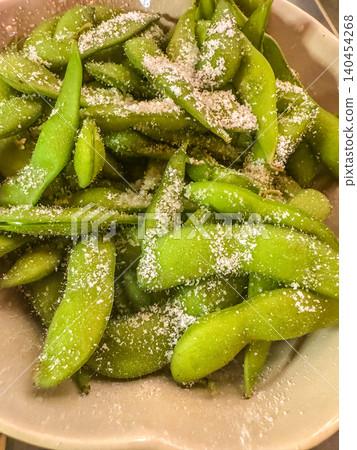 Close up of healthy Japanese appetizer steamed green edamame soybeans in pods generously sprinkled with coarse sea salt in a bowl. 140454268