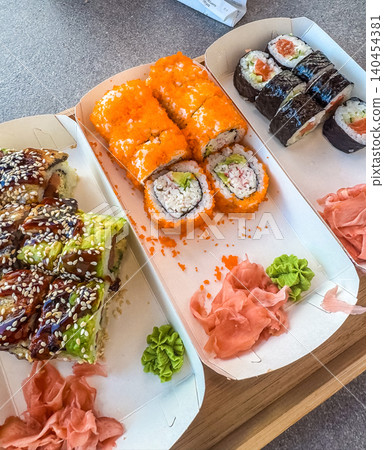 Assorted sushi set in takeaway paper boxes. California rolls with masago, unagi eel rolls, and salmon maki with ginger and wasabi. Assorted sushi set in takeaway paper boxes. California rolls with masago, unagi eel rolls, and salmon maki with ginger and wasabi. 140454381