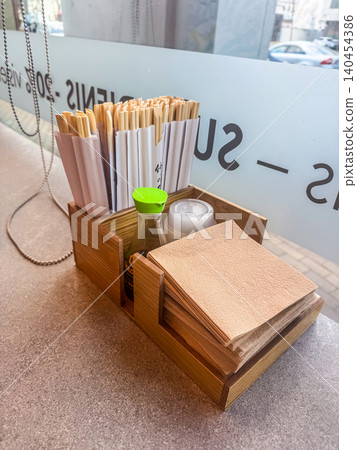 Wooden organizer with chopsticks, soy sauce bottle, napkins on restaurant counter near window. Asian dining tabletop setup. Wooden organizer with chopsticks, soy sauce bottle, napkins on restaurant counter near window. Asian dining tabletop setup. 140454386