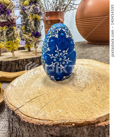 Traditional hand-painted blue Easter egg on rustic wood slice. Folk art margutis ornament with dried flowers background. Traditional hand-painted blue Easter egg on rustic wood slice. Folk art margutis ornament with dried flowers background. 140454395