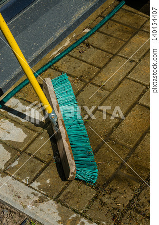 Outdoor Cleaning Concept: Turquoise Industrial Broom Sweeping Wet Stone Pavement Tiles with Garden Hose in the Background Outdoor Cleaning Concept: Turquoise Industrial Broom Sweeping Wet Stone Pavement Tiles with Garden Hose in the Background 140454407