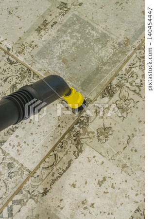 A top-down close-up photo showing a black and yellow steam cleaner brush attachment scrubbing dirty grout lines between patterned ceramic floor tiles. High quality photo A top-down close-up photo showing a black and yellow steam cleaner brush attachment scrubbing dirty grout lines between patterned ceramic floor tiles. High quality photo 140454447
