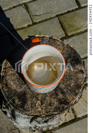 Top view of a ceramic mug on a rustic birch wood log stump during a morning break on a sunny outdoor stone garden patio. Top view of a ceramic mug on a rustic birch wood log stump during a morning break on a sunny outdoor stone garden patio. 140454451