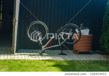 Mountain bike turned upside down for repair and maintenance on a stone patio outside a modern black garden shed or garage. Mountain bike turned upside down for repair and maintenance on a stone patio outside a modern black garden shed or garage. 140454453