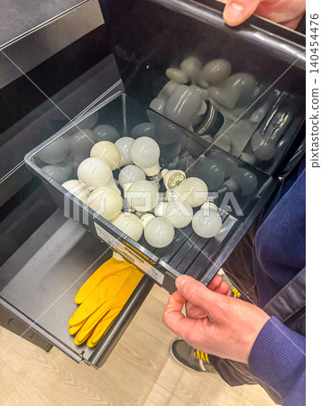 Person Holding Tray of Light Bulbs Over Storage Drawer with Yellow Gloves in Workshop or Garage for Home Maintenance Organization Person Holding Tray of Light Bulbs Over Storage Drawer with Yellow Gloves in Workshop or Garage for Home Maintenance Organization 140454476