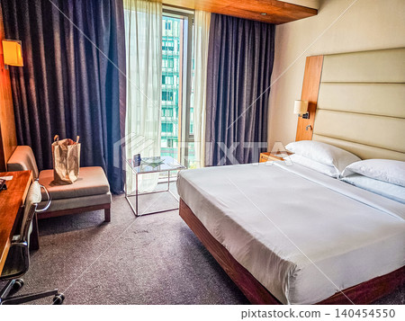 Modern hotel room interior with large bed desk chair window city view curtains cozy accommodation travel hospitality bedroom 140454550