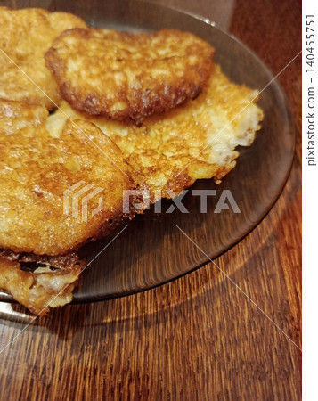 Golden brown potato pancakes, also known as latkes or draniki, fresh from frying and arranged on a dark plate, resting on a textured wooden table 140455751
