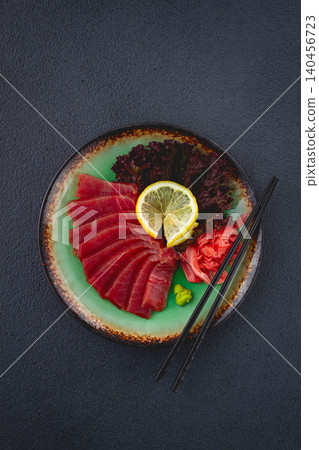 Fresh tuna sashimi served with lemon, wasabi, and pickled ginger on a dark background Fresh tuna sashimi served with lemon, wasabi, and pickled ginger on a dark background 140456723