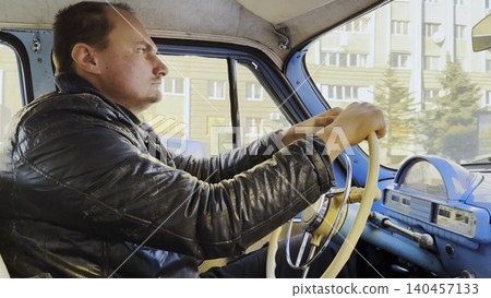 Male driver riding on blue vintage auto at city road on sunny day. Serious man driving retro vehicle at urban street. Confident guy moving in his old auto on route. Slow motion Male driver riding on blue vintage auto at city road on sunny day. Serious man driving retro vehicle at urban street. Confident guy moving in his old auto on route. Slow motion 140457133