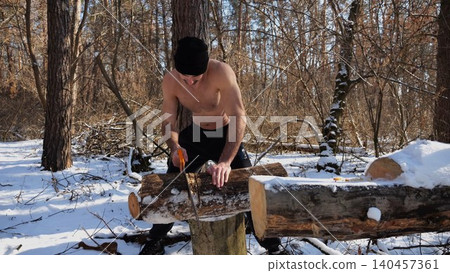 Shirtless man sawing a log in sunny winter forest. Strong guy working with saw in snowy woodland. The scene highlights human effort and outdoor activity in cold conditions. Slow mo 140457361