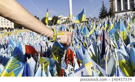 Female hand holding small flag of Ukraine and examining names of the dead war against russia. Memorial of the fallen soldiers, children, women in the center of Kyiv. Concept of tragedy and misfortune Female hand holding small flag of Ukraine and examining names of the dead war against russia. Memorial of the fallen soldiers, children, women in the center of Kyiv. Concept of tragedy and misfortune 140457374