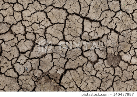 Cracked earth reveals dry, brittle soil. Deep fissures spread across the parched surface. Color shifts from beige to darkened cracks. Texture shows erosion and aridity's force 140457997