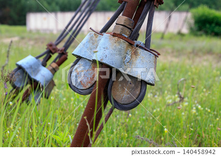 Guy wire anchor with heavy steel cables and rusty turnbuckle, utility pole support assembly close up in green grass Guy wire anchor with heavy steel cables and rusty turnbuckle, utility pole support assembly close up in green grass 140458942