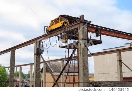 Overhead gantry crane structure on concrete pillars, industrial hoist beam system at factory yard against cloudy sky Overhead gantry crane structure on concrete pillars, industrial hoist beam system at factory yard against cloudy sky 140458945
