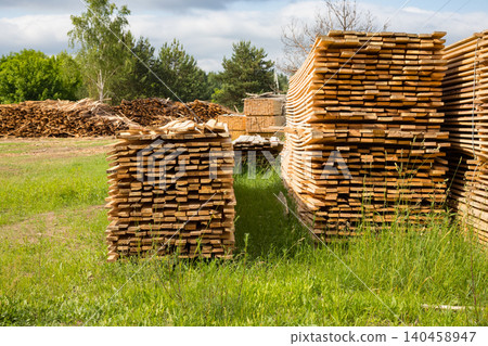Stacked wooden planks at lumber industry yard, sawn timber boards stored at sawmill enterprise outdoor on grass 140458947