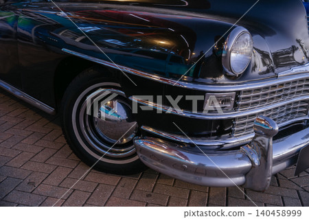 Black vintage classic car with chrome grille, round headlight, and polished bumper parked outdoors at sunset. Retro automobile showcases elegant transportation design and historic automotive Black vintage classic car with chrome grille, round headlight, and polished bumper parked outdoors at sunset. Retro automobile showcases elegant transportation design and historic automotive 140458999