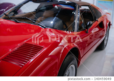 Close-up shot highlights shiny red bodywork of vintage sports car. Distinctive hood vents and windshield wipers are visible, along with a glimpse of tan interior and another vehicle in background. Close-up shot highlights shiny red bodywork of vintage sports car. Distinctive hood vents and windshield wipers are visible, along with a glimpse of tan interior and another vehicle in background. 140459049
