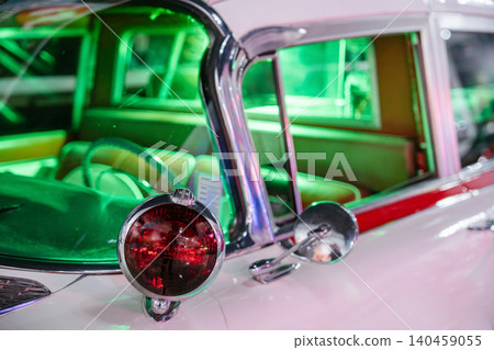 Close-up shot highlights exterior of vintage car showcasing chrome accents and round red taillight. Interior illuminated by vibrant green light reveals plush seating, evoking retro nostalgia. Close-up shot highlights exterior of vintage car showcasing chrome accents and round red taillight. Interior illuminated by vibrant green light reveals plush seating, evoking retro nostalgia. 140459055