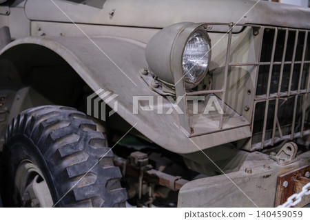 Detailed low-angle view captures front-right section of vintage military vehicle. Textured tire and robust headlight assembly highlight rugged design and historical significance. Detailed low-angle view captures front-right section of vintage military vehicle. Textured tire and robust headlight assembly highlight rugged design and historical significance. 140459059